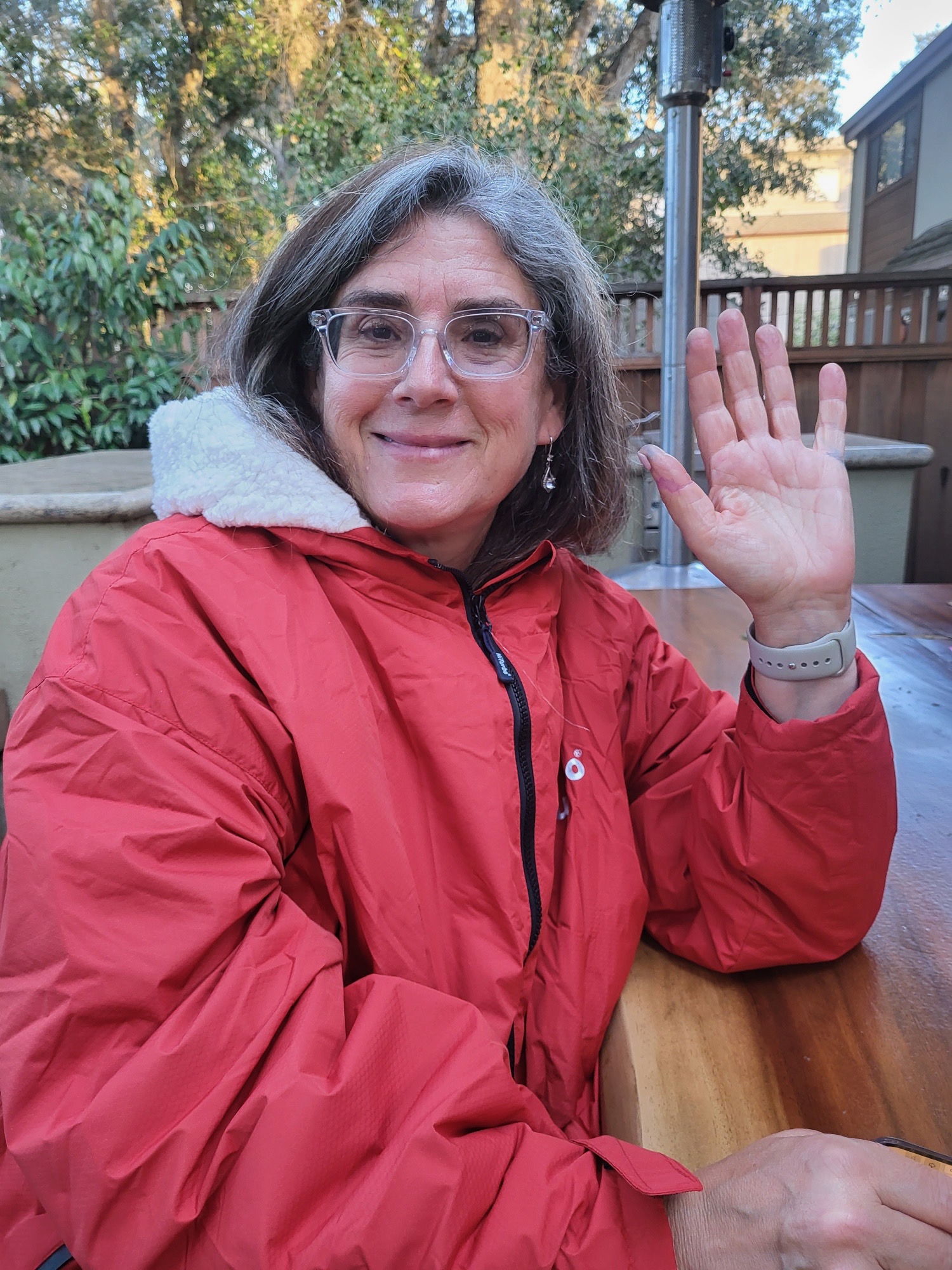 Sara Wildavsky smiling and waving outdoors in a red coat